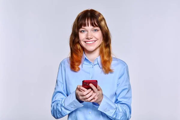 Beautiful smiling teenage female with smartphone in her hands looking at camera —  Fotos de Stock