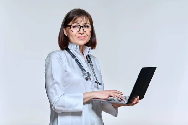Portrait of female doctor using laptop, on light studio background — Stock fotografie