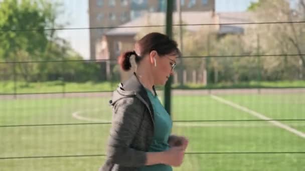 Зріла активна жінка працює на відкритому повітрі, біля стадіону, вид з профілю — стокове відео