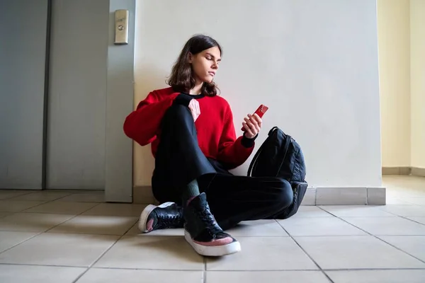Підліток модний чоловік з рюкзаком зі смартфона сидить на підлозі — стокове фото