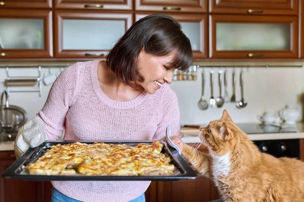 Woman with sheet of baked meat and funny ginger domestic cat