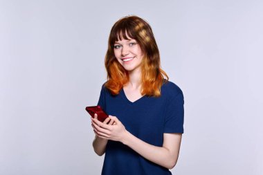 Elinde akıllı telefonuyla kameraya bakan güzel, gülümseyen genç bir bayan.