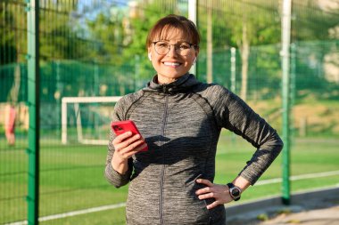 Portrait of smiling middle aged woman looking at camera at sports outdoor stadium clipart