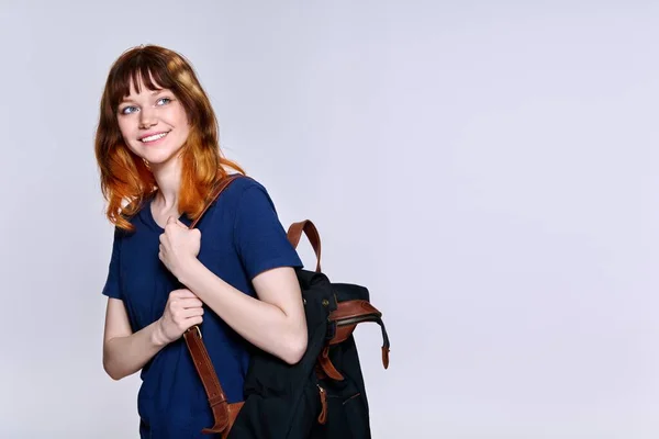 Positive teenage female student with backpack looking away on light studio background — Stockfoto