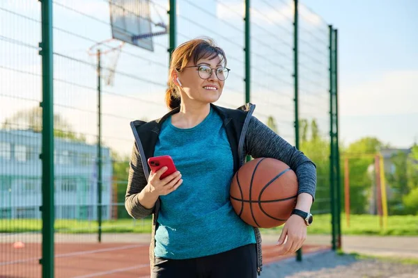Basketbol topu ve akıllı telefonu olan aktif olgun bir kadın.