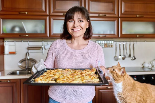 Mujer con hoja de carne al horno y divertido jengibre gato doméstico — Foto de Stock