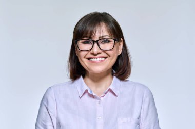 Portrait of middle aged woman looking at camera, on light studio background