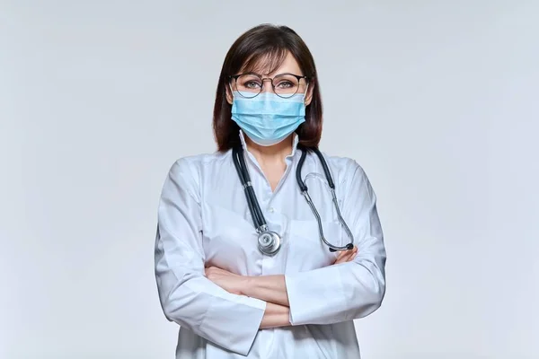 Portrait of female doctor in medical mask looking at camera on light studio background — Stock fotografie