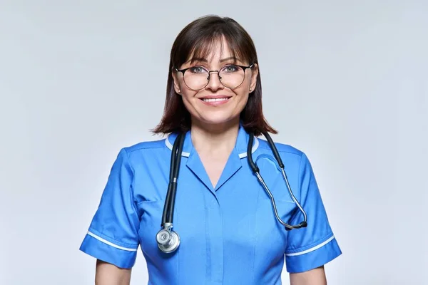 Headshot retrato de enfermeira em uniforme azul olhando para a câmera no fundo do estúdio de luz — Fotografia de Stock