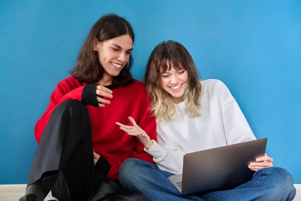 Couple of teenage students using laptop sitting on the floor on blue background — Photo
