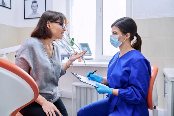 Відвідування стоматологічного кабінету, розмова пацієнта з лікарем, нотатки стоматолога — стокове фото