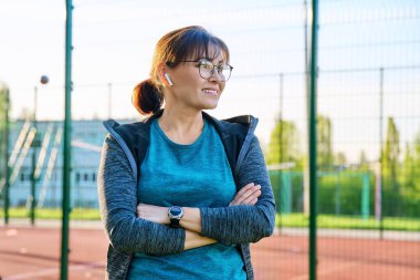 Profilde görünen, gülümseyen orta yaşlı bir kadının açık hava portresi.