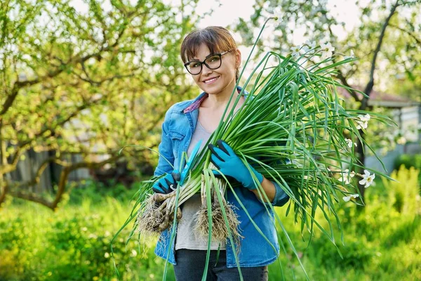 Beyaz nergis çalısı ve kürekle bahçe eldivenleri giymiş bir kadın kameraya bakıyor.