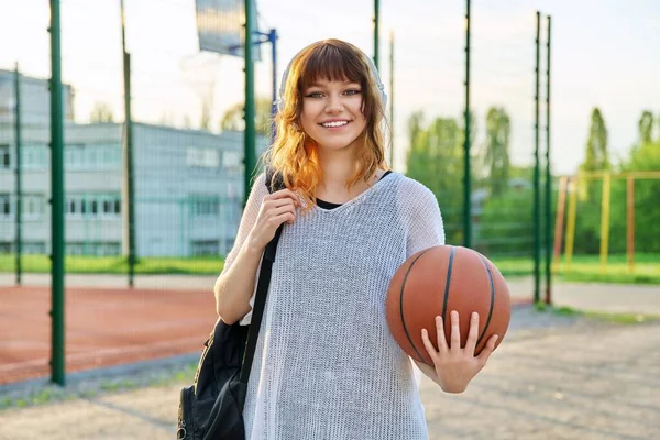 Sırt çantalı, basketbol topu tutan kulaklıklı güzel bir kız öğrenci.
