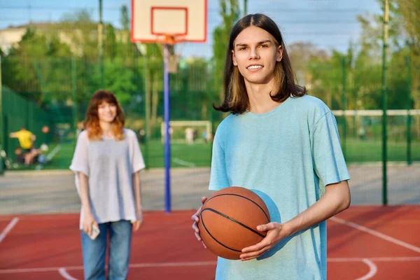 屋外ゲームコートでバスケットボールをしている若い男の肖像画、女の子は焦点を当てていません. — ストック写真