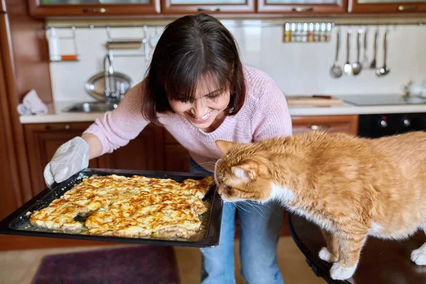 Woman with sheet of baked meat and funny ginger domestic cat