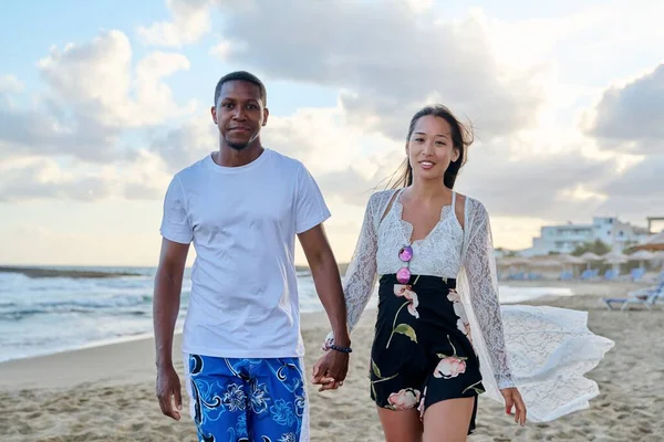 Young happy couple walking on the beach holding hands.