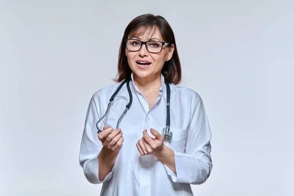 Portrait of female doctor looking at camera talking gesturing on light studio background — Stock Photo, Image