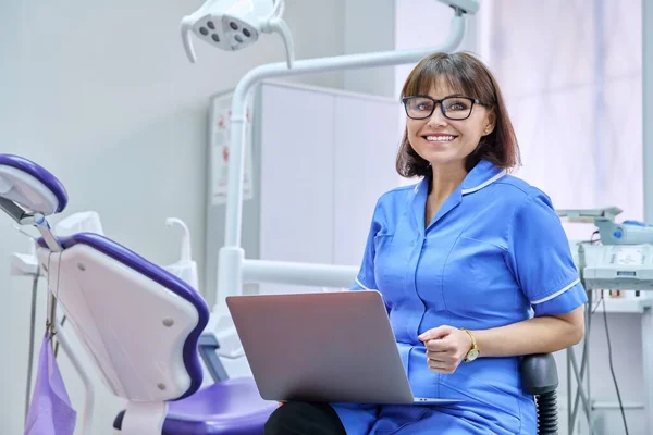 Портрет стоматолога медсестри, сидячи в офісі з ноутбуком в руках, дивлячись на камеру — стокове фото