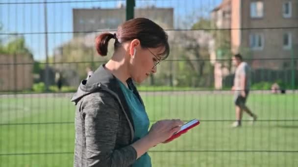 Ενεργή ώριμη γυναίκα σε αθλητικά ρούχα με smartphone, εξωτερική, προβολή προφίλ — Αρχείο Βίντεο