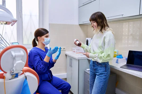 Dentista che somministra medicine per denti e cavità orale in bottiglia a giovani donne in ufficio — Foto Stock
