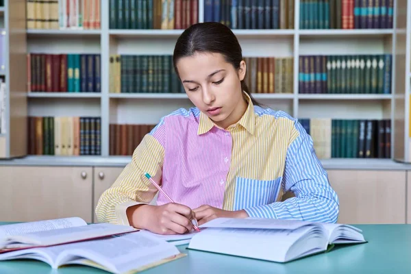 在学校图书馆学习的少女学生 女性坐在书桌前看书 用笔记本写作 青少年概念 — 图库照片
