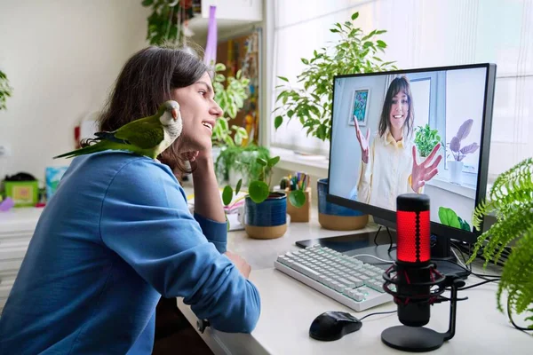 Online meeting of teenagers friends, guy with pet parrot sitting at home talking to a smiling female on computer monitor. Friendship, communication, technology, youth, lifestyle, young people concept