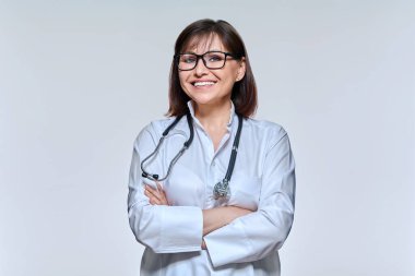 Steteskop ile beyaz üniformalı gülümseyen kadın doktor portresi, stüdyo arka planında çapraz kolları olan kendine güvenen doktor. Meslek, tıp, sağlık