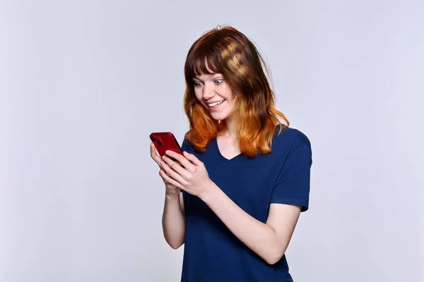 漂亮的少女微笑着看着智能手机屏幕 背景轻松 一个红头发的女孩 手里拿着手机Lifestyle Technology Communication Youth Young People — 图库照片