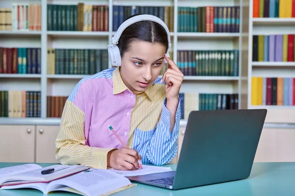 高中女生戴耳机 在学校图书馆读书 使用书本和笔记本电脑 青少年概念 — 图库照片