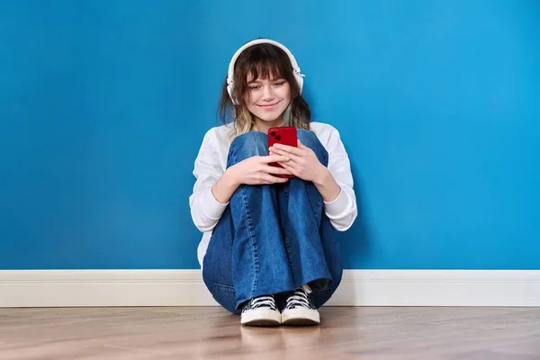 Όμορφη Έφηβη Γυναίκα Ακουστικά Smartphone Κάθεται Στο Πάτωμα Μπλε Φόντο — Φωτογραφία Αρχείου