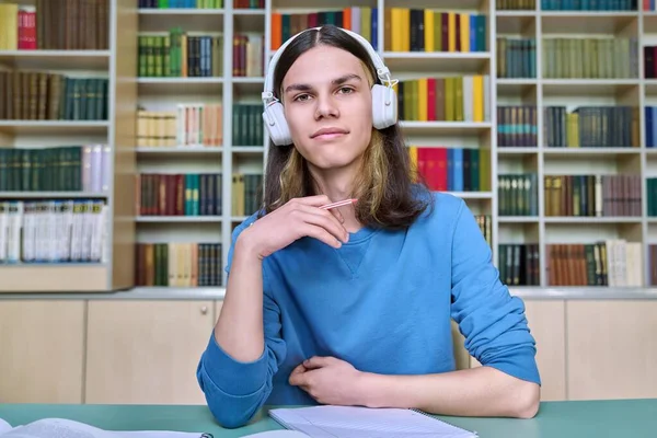 Kulaklıklı genç bir üniversite öğrencisi web kamerasına bakıyor, kütüphanedeki masada oturuyor. Video konferans sohbeti yapan, uzaktan ders çalışan, online sınava giren bir adam. Eğitim, teknoloji