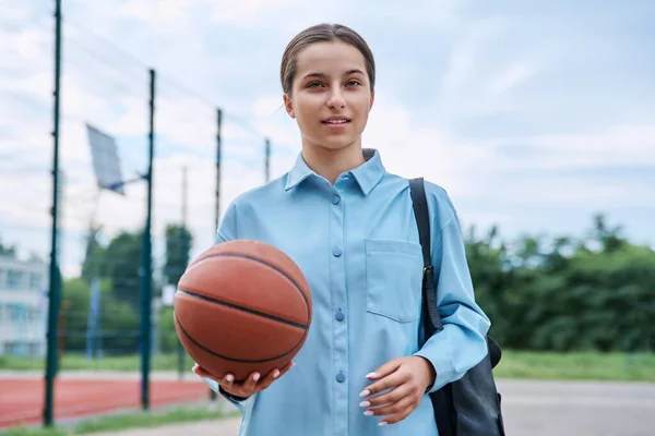 照片上的十几岁的女生背着背包和篮球 看着镜头 靠近篮球场的室外球场 积极健康的体育生活方式 青春期 学校观念 — 图库照片
