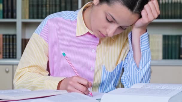 学校の図書館で勉強している10代の女子学生 女性は机に本を置き ノートに書いて座っている 青年期の概念 — ストック動画