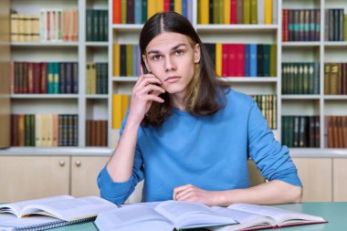 Üniversite kütüphanesinde okuyan, defter yazan, kitap okuyan, kameraya bakan yakışıklı bir erkek. Eğitim, bilgi, üniversite, üniversite konsepti