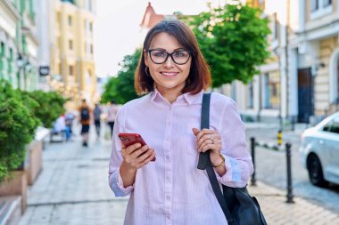Orta yaşlı, gülümseyen bir kadın. Şehir caddesinde kameraya bakıyor. Açık havada başarılı, başarılı, olgun bir iş kadını. İş, yaşam tarzı, şehir tarzı, 40 'lı yaşlardaki insanlar kavramı