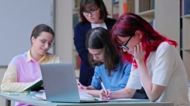 Kütüphanede okuyan bir grup genç öğrenci, dizüstü bilgisayar kullanan ve not defterine yazı yazan, öğrencilere yardım eden öğretmenler. Üniversite, lise, eğitim öğrenme konsepti