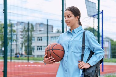 Sırt çantalı ve basketbol toplu genç kız portresi, basketbol sahasının yanında, fotokopi alanı. Aktif sağlıklı spor yaşam tarzı, ergenlik, okul konsepti