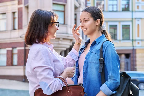 Talking mom and teenage daughter outdoors, on a city street. Parents and child teenager laughing, smiling, walking together. Family, two generations, lifestyle, leisure, people concept