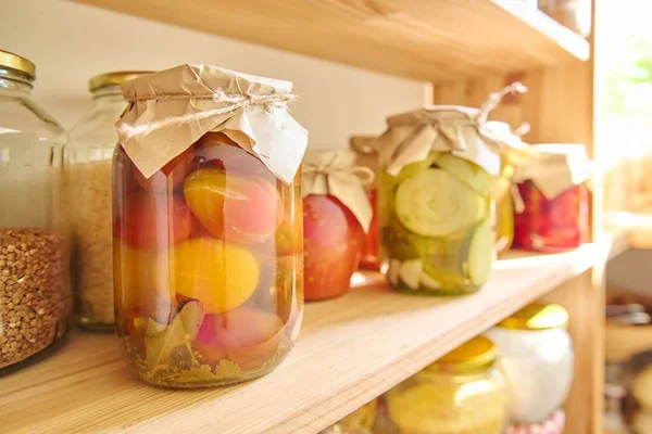 Storage of food in the kitchen in pantry. Pickled canned vegetables and fruits on the shelf, jar of tomatoes close-up. Cooking at home, homemade preservation, household