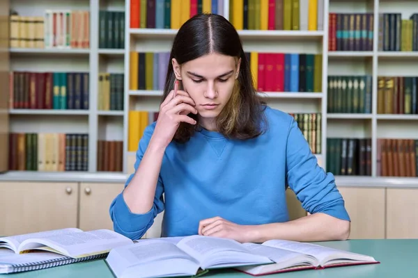 Teenage guy studying in the college library, writing in a notebook reading books. Education, knowledge, college, university concept