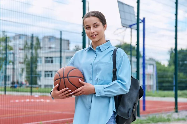 照片上的十几岁的女生背着背包和篮球 看着镜头 靠近篮球场的室外球场 积极健康的体育生活方式 青春期 学校观念 — 图库照片