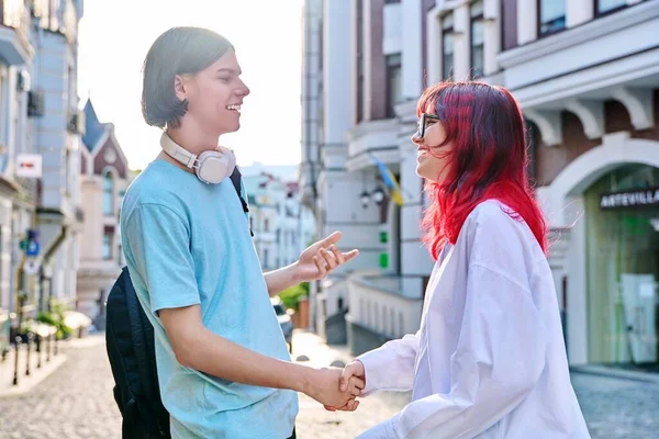 Meeting, shaking hands teenage male and female friends on the city street. Fashionable having fun teenagers guy and girl together. Friendship, communication, holidays, lifestyle, youth, urban style