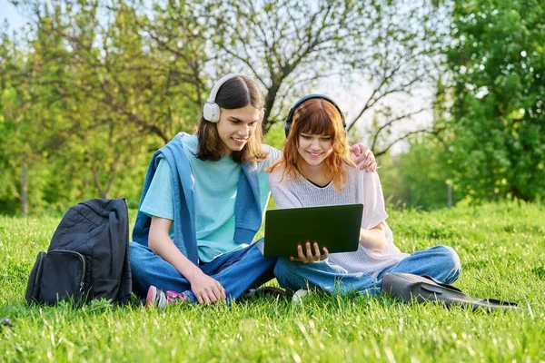 バックパック付きのヘッドフォンで2人の友人の学生 男と女の子 ノートパソコンを見て 草の上に座っている コミュニケーション 若者の概念 — ストック写真