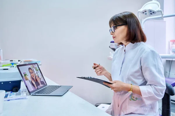 Video chat call conference of doctor dentist and young woman patient on laptop screen, in dental office. Online meeting, consultation, service, dentistry, medicine, technology concept