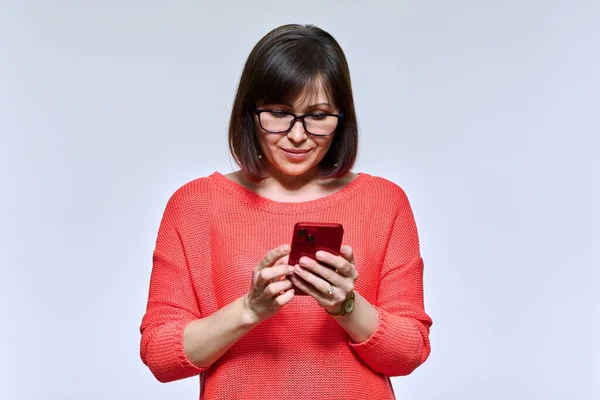 中年妇女微笑着看着智能手机的光工作室背景 漂亮的情绪女性使用移动在线应用程序 生活方式 互联网 40多岁人口的概念 — 图库照片