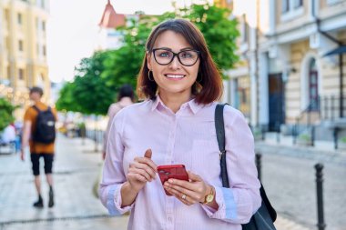 Orta yaşlı, gülümseyen bir kadın. Şehir caddesinde kameraya bakıyor. Açık havada başarılı, başarılı, olgun bir iş kadını. İş, yaşam tarzı, şehir tarzı, 40 'lı yaşlardaki insanlar kavramı