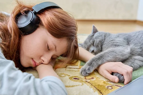 Preteen girl in headphones sleeping with cat on the floor at home. Young owner and gray British pet sleep together. Animals, love, friendship, children, lifestyle concept