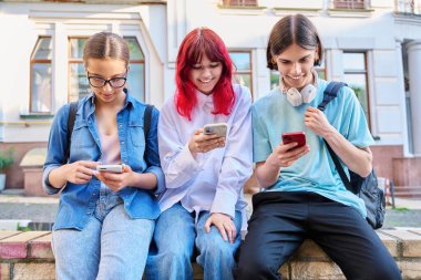 Genç arkadaşlar birlikte şehir sokaklarında akıllı telefonları kullanarak eğleniyorlar. Teknoloji mobil uygulamaları, yaşam tarzı, tatil eğlencesi, şehir tarzı, gençlik kavramı
