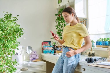 Akıllı telefon kullanan mutlu genç bayan, evde dinleniyor, kopyalama uzayı. Yaşam tarzı, ergenlik, teknoloji, internet, sosyal medya, gençlik kavramı